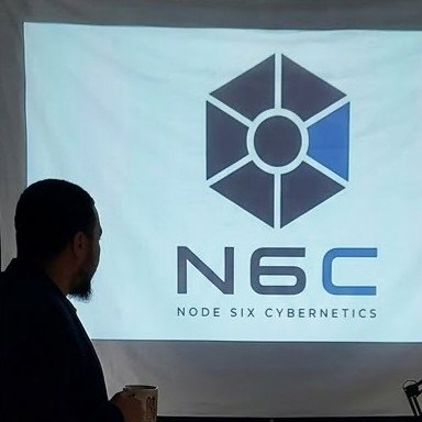 Anderson Silva em silhueta, segurando uma caneca, diante do logotipo da N6C projetado na parede